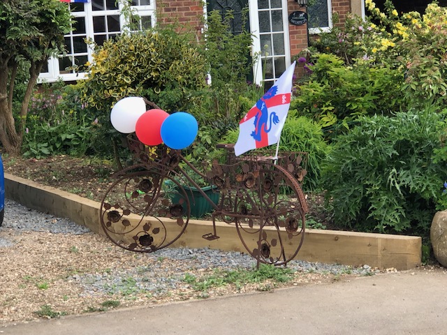 A rusty looking bicycle is decorated with red, white and blue balloons.